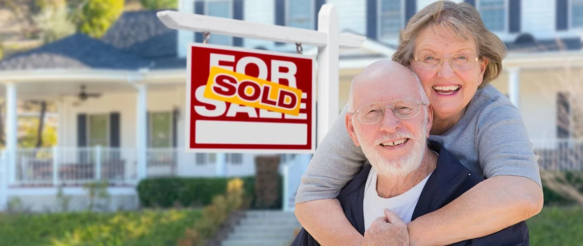Older couple in front of a for sale sign