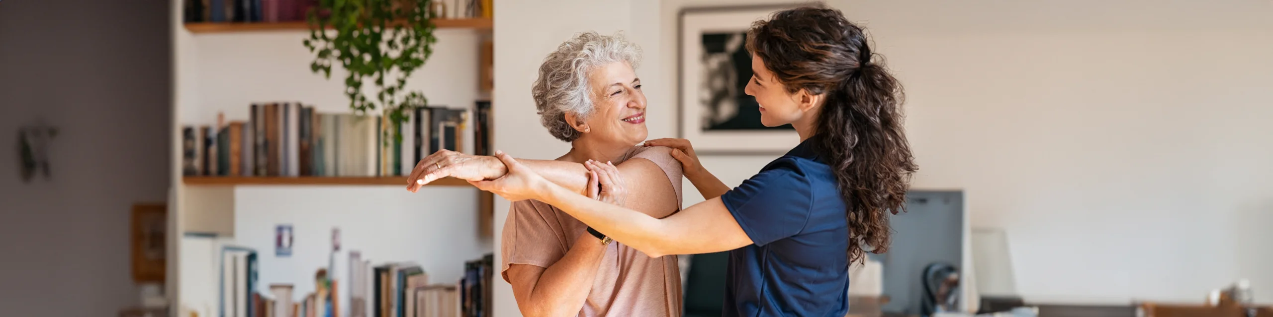Senior woman smiling at a caretaker in bright living room