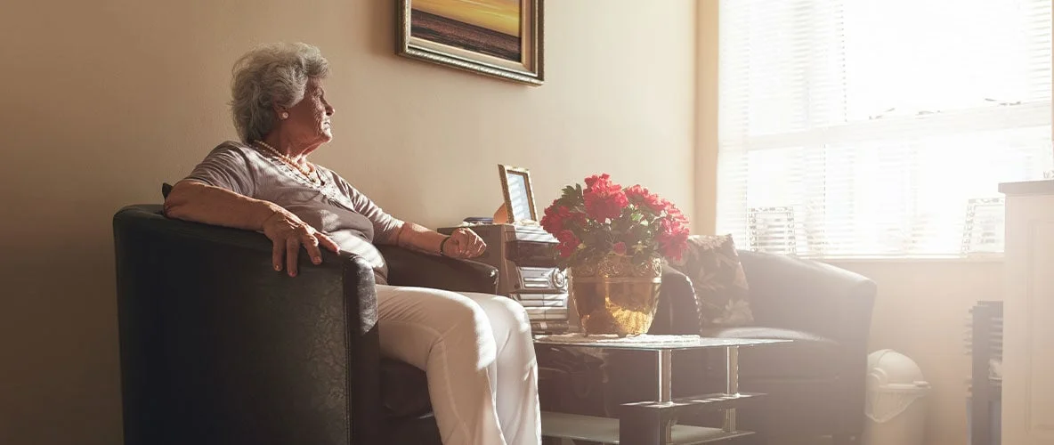Older adult sitting quietly in softly lit room staring out the window
