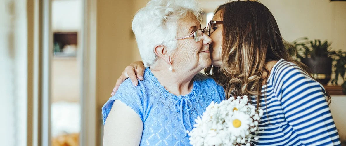 Loved one kissing senior woman’s cheek during supportive visit